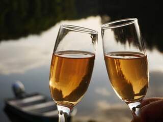 Two glasses with rose champagne wine in hands, Romantic lake as background