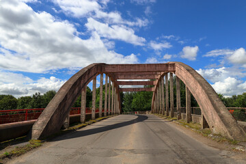 Old arched reinforced concrete road bridge against the background of blue sky and white clouds. Sovetsk, Kaliningrad region