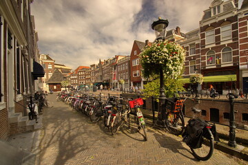 Fototapeta na wymiar Ein Straße an einem Gracht in Utrecht mit viele Häuser, vielen Fahrräder und Strassen Laternen mit unzählige weiße und rote Blumen unter dem blauen Himmel mit weißen Wolken.