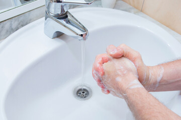 Man washing hands with soap under bathroom sink.