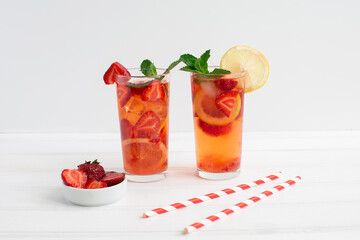 Cold strawberry lemonade juice with ice cubes, lemon, cocktail tube and mint.