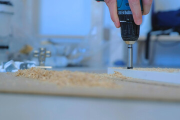 Man drills a round hole in the chipboard making furniture wardrobe door, closeup view. Guy is...