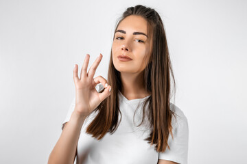 Good job. Pretty carefree modern stylish European girl with long chestnut hair making OK gesture as if saying that everything is finee, white background