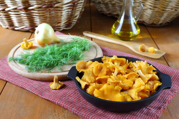 A fresh chanterelles mushrooms in a cast iron pan before cooking are near the plate with onion and...