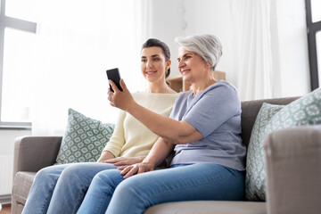 family, generation and people concept - happy smiling senior mother with adult daughter taking selfie by smartphone at home