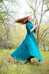 Beautiful bootless woman dance in forest. Barefoot girl in elegant blue dress posing in forest on green trees background. Fun and joyful concept.