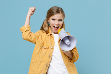 Joyful little blonde kid girl 12-13 years old in yellow jacket posing isolated on pastel blue background. Childhood lifestyle concept. Mock up copy space. Screaming in megaphone doing winner gesture.