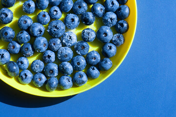 Part of a yellow round plate in which blueberries with sugar lie