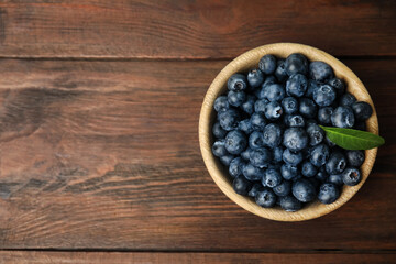 Tasty ripe blueberries in bowl on wooden table, top view. Space for text