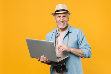 Smiling traveler tourist elderly gray-haired man isolated on yellow background. Passenger traveling abroad on weekend getaway. Air flight journey concept. Work on laptop computer, booking taxi, hotel.