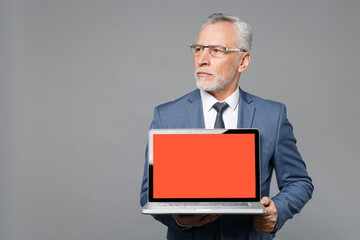 Serious elderly gray-haired business man in blue suit shirt tie isolated on grey background. Achievement career wealth business concept. Hold laptop pc computer with blank empty screen looking aside.