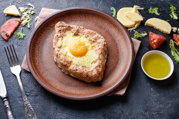 Fresh khachapuri with wholegrain flour, cottage cheese, egg, sulugini cheese, vegetables, butter, greens, plate, fork knife