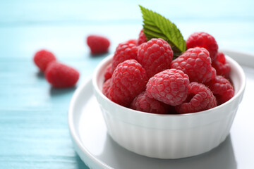Delicious ripe raspberries in bowl on light blue wooden table, closeup
