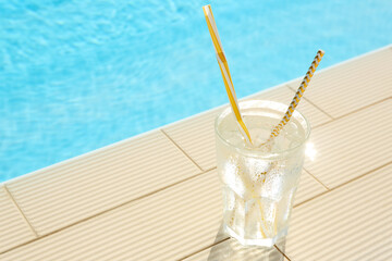 Glass of refreshing drink near swimming pool. Space for text