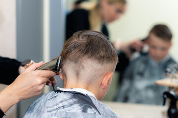 Back view Close up caucasian pretty school boy trendy haircut at bright modern barbershop.