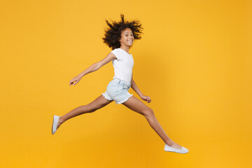 Fototapeta na wymiar Full length portrait of smiling little african american kid girl 12-13 years old in white t-shirt isolated on yellow wall background studio portrait. Childhood lifestyle concept. Jumping, having fun.
