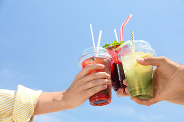 People with refreshing drinks against blue sky, closeup