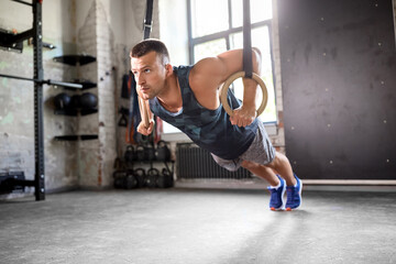Fototapeta na wymiar fitness, sport, bodybuilding and people concept - young man doing push-ups on gymnastic rings in gym