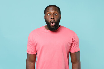 Shocked young african american man guy in casual pink t-shirt posing isolated on blue background studio portrait. People sincere emotions lifestyle concept. Mock up copy space. Keeping mouth open.