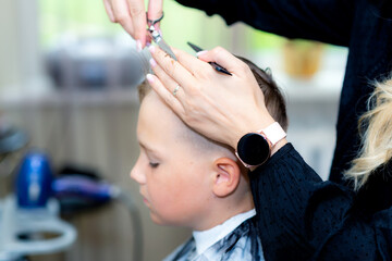 Serious school boy ready getting trendy haircut from expirienced barber at fashionable hairdressing salon.