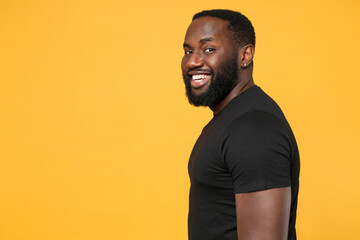 Side view of smiling african american man guy football fan in casual black t-shirt isolated on yellow background studio portrait. People emotions lifestyle concept. Mock up copy space. Looking camera.