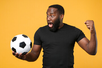 Shocked african american man guy football fan in black t-shirt isolated on yellow background. Sport...