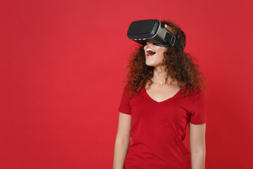 Excited young african american woman girl in casual t-shirt posing isolated on red wall background studio portrait. People lifestyle concept. Mock up copy space. Watching in headset, looking aside.