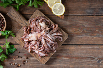 The tentacles of squid. Raw squid tentacles on a wooden serving Board on a brown wooden kitchen table. Lots of squid tentacles. The view from the top