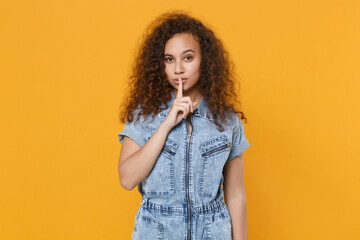 Secret young african american woman girl in casual denim clothes isolated on yellow background studio. People lifestyle concept. Mock up copy space. Say hush be quiet with finger on lips shhh gesture.