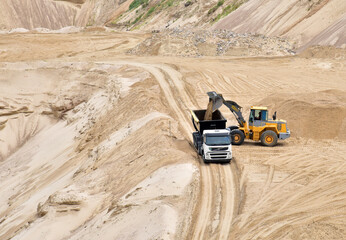 Wheel front-end loader loading sand into heavy dump truck at the opencast mining quarry. Dump truck transports sand in open pit mine. Quarry in which sand and gravel is excavated from the ground.