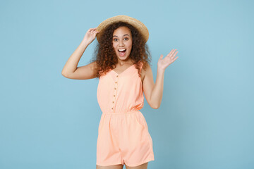 Excited young african american woman girl in pastel summer clothes hat posing isolated on blue wall background studio portrait. People emotions lifestyle concept. Mock up copy space. Spreading hands.