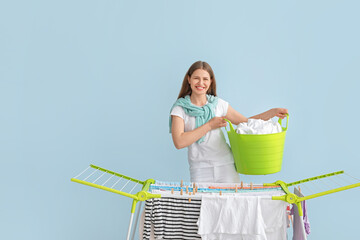 Woman hanging clean clothes on dryer against color background