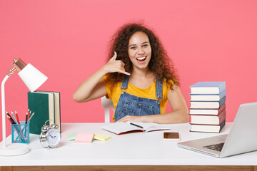 Funny african american girl employee in office sit isolated on pink background. Achievement business career. Education in school university college concept. Doing phone gesture like says call me back.