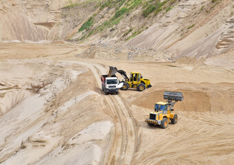 Obraz na płótnie Canvas Wheel front-end loader loading sand into heavy dump truck at the opencast mining quarry. Dump truck transports sand in open pit mine. Quarry in which sand and gravel is excavated from the ground.