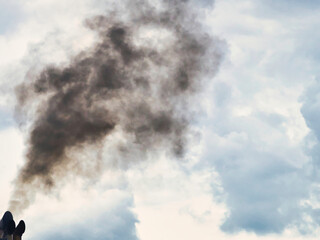 Fototapeta na wymiar Huge plume of black smoke from fire rising high above flat land against cloud sky