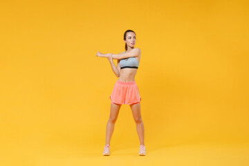 Full length portrait strong fitness woman in sportswear working out isolated on yellow background. Workout sport motivation lifestyle concept. Mock up copy space. Doing stretching exercising for arms.