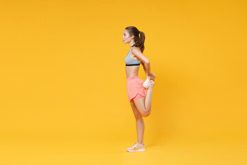 Full length portrait strong fitness woman in sportswear working out isolated on yellow background. Workout sport motivation lifestyle concept. Mock up copy space. Doing stretching exercising for legs.