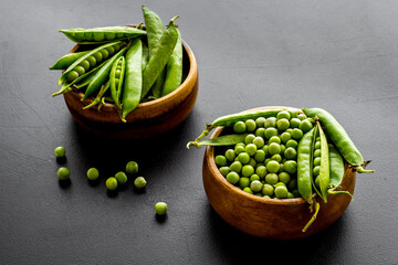 Set of green pea pods in wooden bowl on kitchen table desk