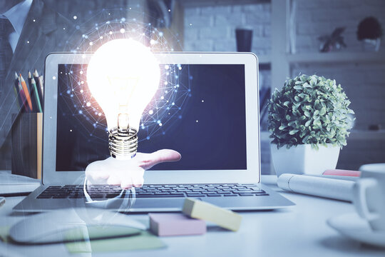 Computer on desktop in office with bulb icon hologram. Double exposure. Concept of idea.