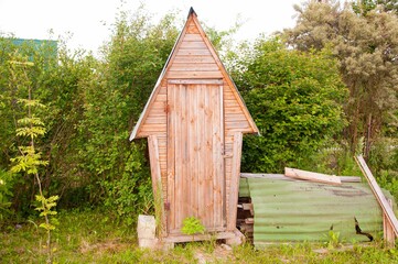 toilet in the garden WC cabin toilet in the form of a wooden cottage house near a countryside road and tall trees.