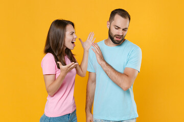 Irritated young couple friends guy girl in blue pink t-shirts posing isolated on yellow background studio portrait. People lifestyle concept. Mock up copy space. Screaming swearing spreading hands.