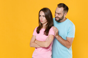 Offended smiling young couple friends guy girl in blue pink t-shirts posing isolated on yellow background studio portrait. People lifestyle concept. Mock up copy space. Holding hands crossed, hugging.