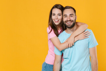 Obraz premium Cheerful young couple two friends guy girl in blue pink t-shirts posing isolated on yellow wall background studio portrait. People sincere emotions lifestyle concept. Mock up copy space. Hugging.