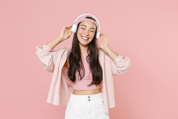 Smiling young asian woman girl in casual clothes cap posing isolated on pastel pink background studio portrait. People emotions lifestyle concept. Mock up copy space. Listening music with headphones.
