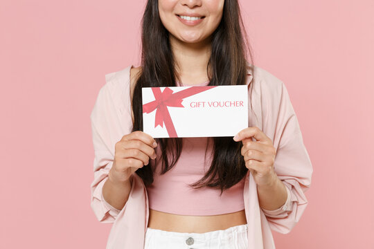 Cropped image of smiling young asian woman girl in casual clothes cap posing isolated on pastel pink background studio portrait. People lifestyle concept. Mock up copy space. Hold gift certificate.