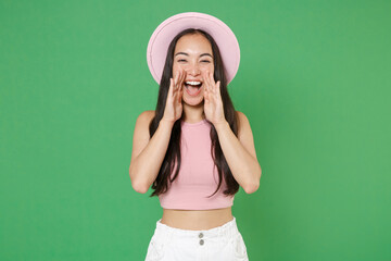 Cheerful young asian woman girl in casual pink clothes hat posing isolated on green background studio portrait. People lifestyle concept. Mock up copy space. Screaming with hands gesture near mouth.