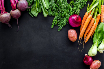Vegetables harvest with green tops on black table top view frame copy space