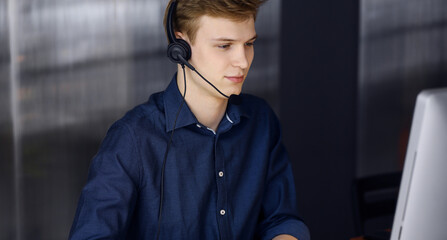 Young blond businessman using headset and computer at work. Startup business means working hard and out of time for success achievement