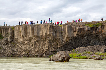 Tourists standing on basalt columns looking at Godafoss waterfall in northern Iceland, low view