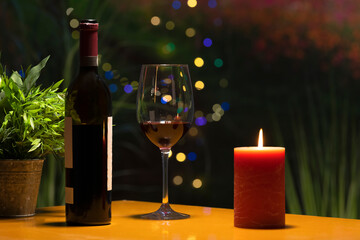 a glass of wine surrounded by a wine bottle and a lit candle on a table. Celebration and holidays...